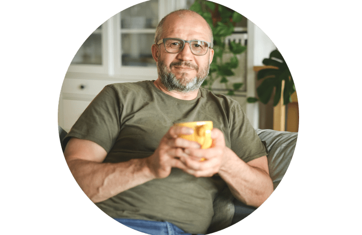 Man in home with cup in hand, looking into camera